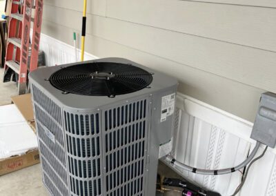 Exterior home air conditioning unit installed beside a house with a ladder leaning against the siding.